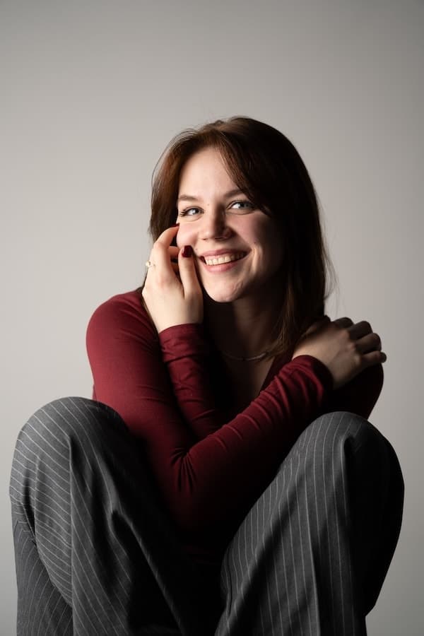 Femme assise en pull bordeaux, souriant devant un fond clair