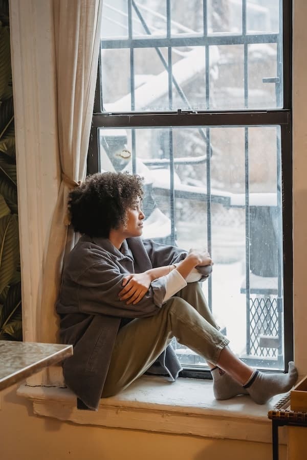 Femme assise près d’une fenêtre, regardant calmement vers l’extérieur