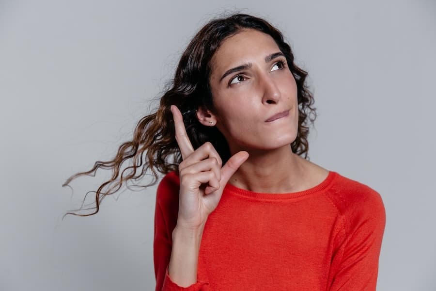 Femme en pull rouge regardant vers le haut, un doigt levé