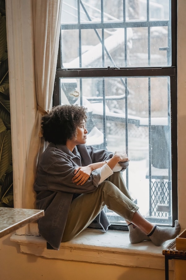 Femme assise près d’une fenêtre, regardant calmement vers l’extérieur